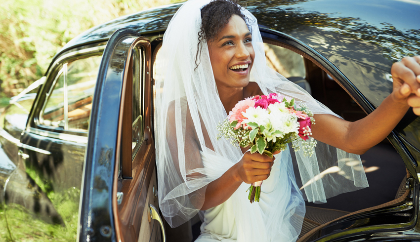 A happy bride exiting her car with a bouquet of flowers.